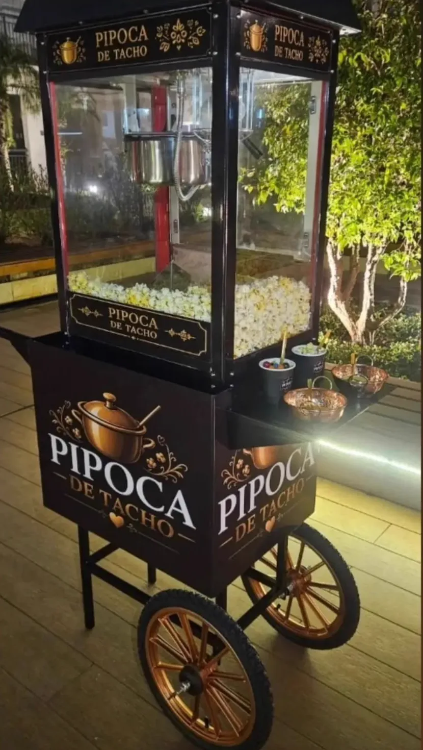 Carrinho vintage preto da Pipoca de Tacho montado à noite, com rodas cobre e vitrine cheia de pipoca
